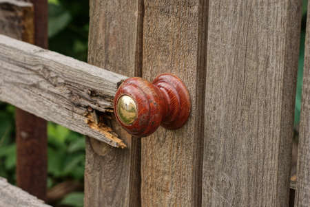 one brown plastic doorknob on the gray wooden boards of an old door on the streetの写真素材