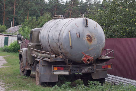 one old gray truck with a barrel stands on the street near the fence