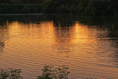 part of the lake with gray water and orange sunset reflections on the evening street