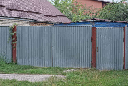 one big gray closed metal gate and door and part of the fence on the street