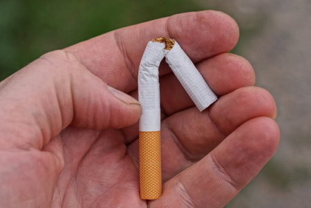 one broken white cigarette with a brown filter lies on the palm of his handの写真素材