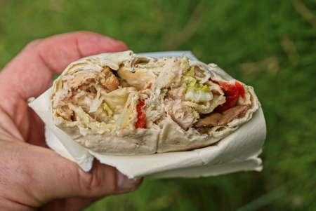 food from a fried piece of shawarma in a paper package in a hand on the street