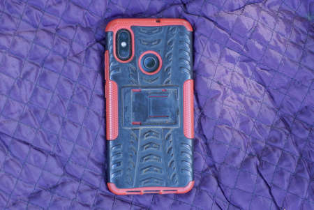 one smartphone in a red black plastic case lies on a purple blanket fabric