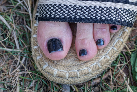 leg of a woman in a gray summer slipper made of fabric with fingers with a black pedicure on her nails on the street in green grassの写真素材