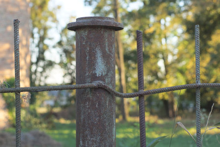 part of an old iron wall of a fence made of brown gray metal pipes and steel bars from fittings on the street against a background of green vegetationの写真素材
