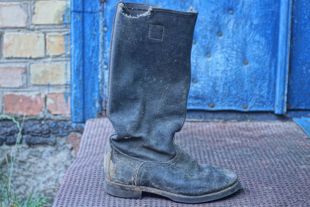 one old black tarpaulin boot stands on a brown threshold near a blue door in the streetの写真素材