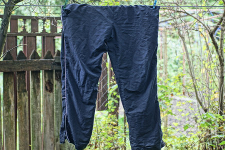 one blue crumpled cloth pants hangs on a wire in the street among green vegetationの写真素材