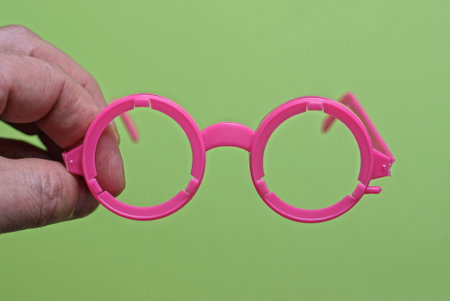 fingers on the hand hold one plastic pink toy glasses on a green backgroundの写真素材