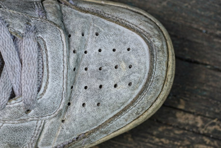 part of one white dirty leather sneaker stands on a gray table