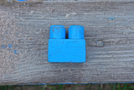 one blue small plastic part from a toy constructor lies on gray sand on a wooden table in the streetの写真素材