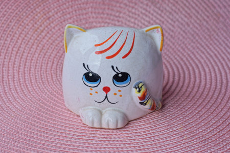 one small ceramic white bank piggy bank with a figure of a cat stands on a pink tableの写真素材
