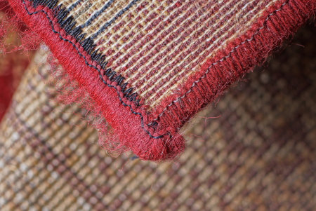 part of a brown floor carpet with an overlock red thread edge