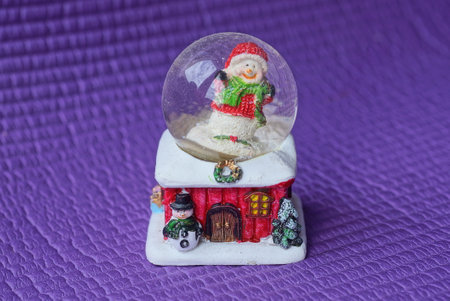 a toy of christmas santa claus in a glass ball on a colored plastic house with a snowman stands on a...