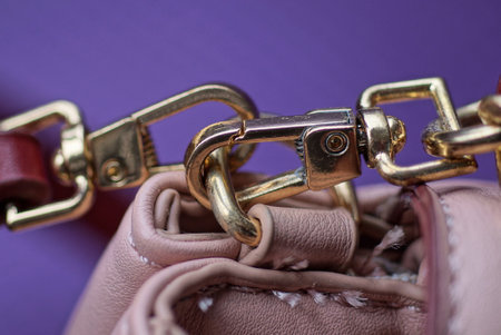yellow metal latch with a ring on the strap of a leather pink bag on a purple backgroundの写真素材