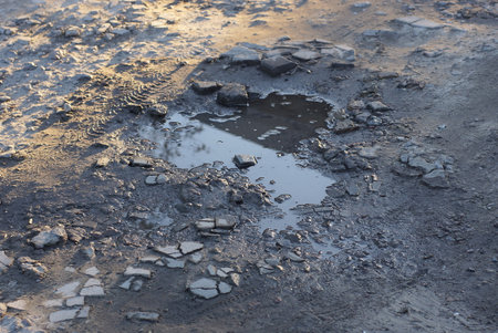 one puddle with dirty water on the gray ground of a rural road in the streetの写真素材