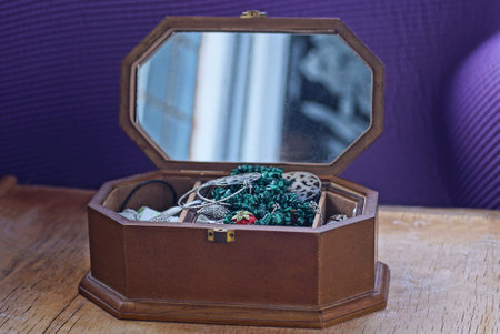 one open large brown wooden box with a mirror full of rings, earrings, bracelets and colored jewelry stands on a lilac tableの写真素材