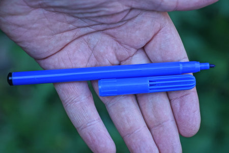one open plastic felt-tip pen with a cap lies on an open palm on a green backgroundの写真素材