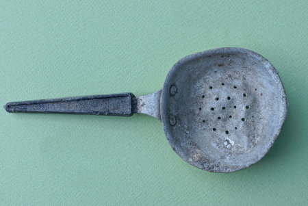 one old dirty crumpled metal gray colander with a black plastic handle lies on a green tableの写真素材