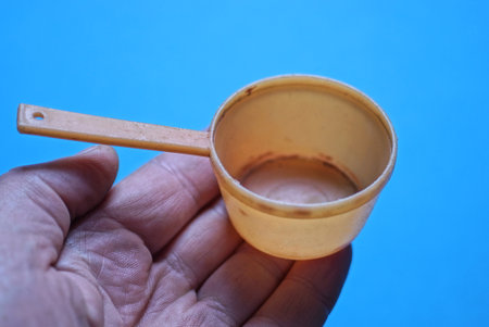 one small toy brown plastic ladle pan lies on the fingers on the hand on a blue backgroundの写真素材