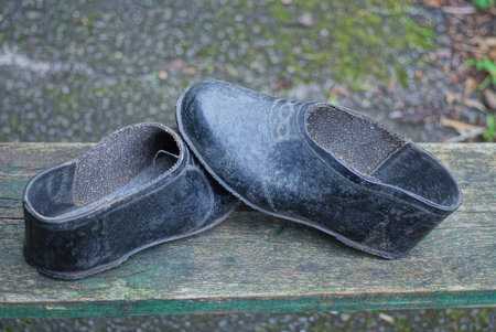 two old black dirty rubber galoshes shoe stands on a gray wooden table in the street