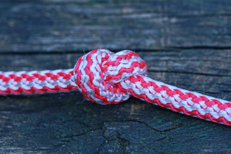 a piece of thick white red rope twine with a knot lies on a gray wooden tableの写真素材