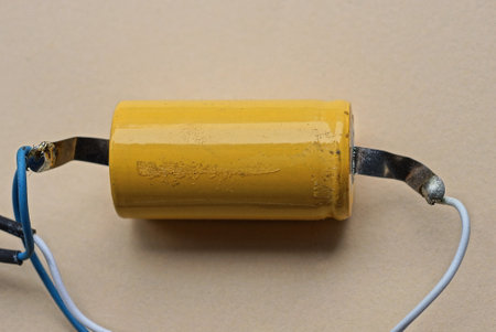 a detail from an old yellow metal resistor with soldered wires lies on a brown table