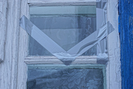part of an old window with a white wooden frame and gray glass with cracks sealed with tape