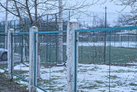 part of a green metal mesh fence wall with concrete pillars on a winter street in white snow and...
