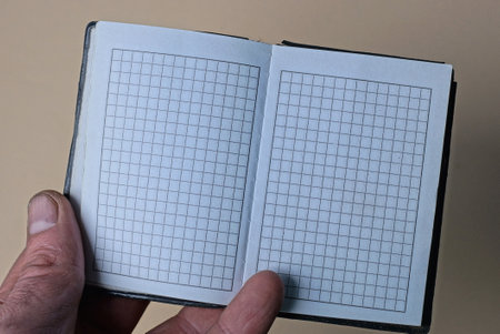hand holding an open small notepad with blank white pages on a brown background