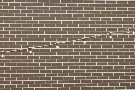 a long electric cable with light bulbs with yellow lighting on the street against a brown brick wall