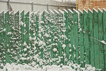 part of the green wall of a wooden fence in white snow on a winter streetの写真素材