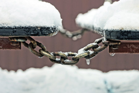 gray iron iced chain on wooden plank wall in white snow on winter street