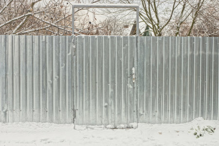 gray closed metal door on an iron fence wall in white snow on a winter street