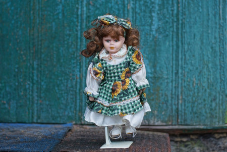 one plastic doll in a colored dress and brown hair stands on a gray table against a green wallの写真素材