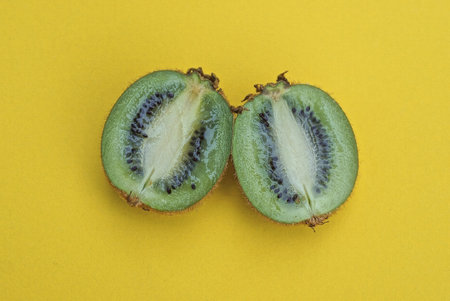two pieces of sliced fresh green kiwi fruit lie on a yellow tableの写真素材