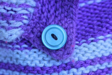 one large blue plastic button on a purple white knitted woolen fabric on a garment