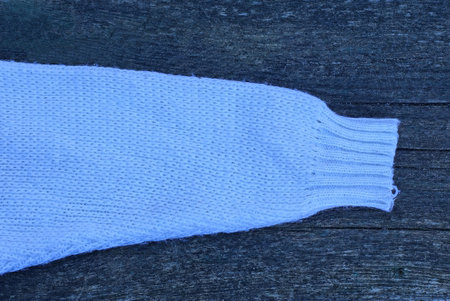 one white woolen knitted sleeve on a sweater lies on a black wooden table