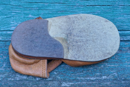 one gray sole of a brown leather shoe with a black heel lies on a green wooden table