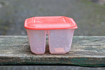 one white plastic grocery box closed with a red lid stands on a gray wooden table in the streetの写真素材