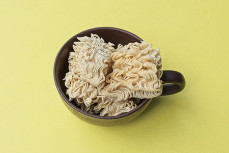pieces of dry vermicelli in a brown cup stands on a yellow tableの写真素材