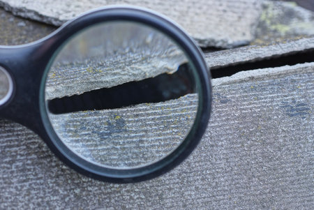 one black magnifier in hand enlarges crack on gray slate concrete wallの写真素材