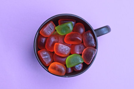 red and green gummy candies lie in a brown cup on a pink tableの写真素材