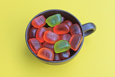 red and green gummy candies lie in a brown cup on a yellow tableの写真素材