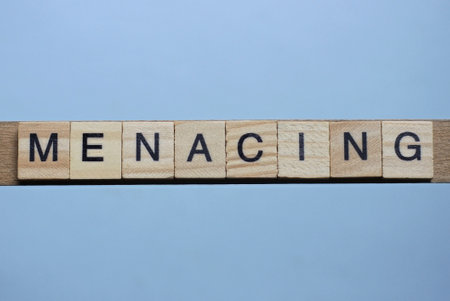 text the word menacing from brown wooden small letters with black font on an gray table