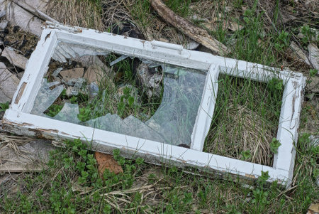 one white old wooden frame with broken glass lies on the green grass in the street