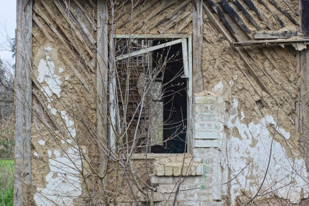 one empty old broken window with a wooden frame on a brown shabby wall of a destroyed house burned down after a fire on the streetの写真素材