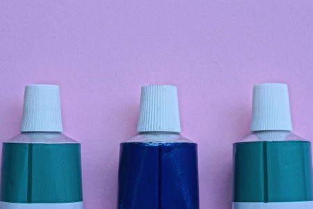 three medical metal green blue tubes with white plastic caps lie on a pink table