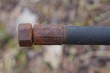 part of an old black plastic hose with a brown rusty iron nut on a gray background outdoors