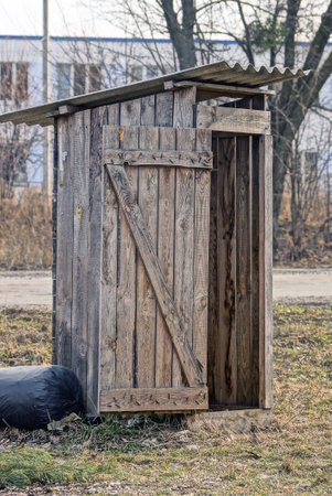 one old gray wooden outdoor rural toilet stands on the ground in green grass in the streetの写真素材
