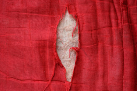 part of an old red torn fabric with a big white holeの写真素材